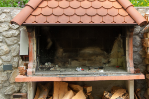 Imagen de una barbacoa de obra al aire libre con leña en el suelo y con algo de suciedad en la zona de elaboración.
