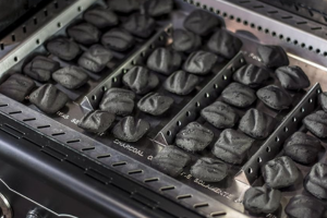 Bandeja con carbón en una barbacoa hibrida, se observan los encendedores de gas.